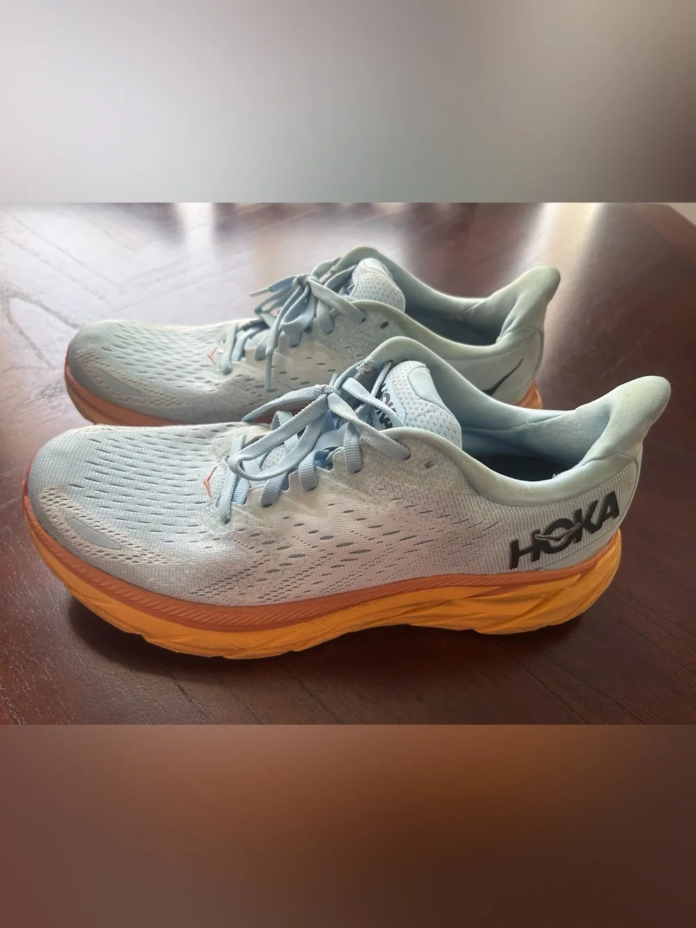 Hoka Women's Pale Blue Running Shoes with Orange Midsole. It has some detail on